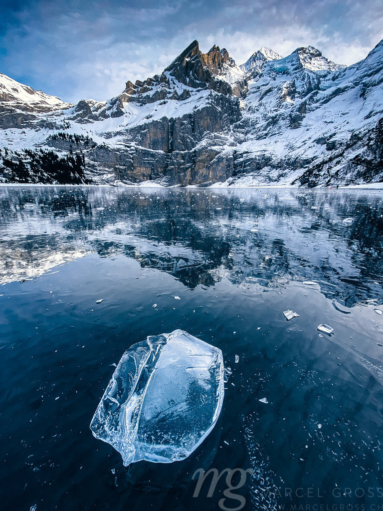 beaufiful clear chunk of ice on frozen lake Oeschinensee with reflection and Blümlisalp Mountains in the Bernese Alps | Die ideale Geschenkidee für Naturliebhaber. Naturbilder von Marcel Gross Photography für ihr Zuhause in den verschiedensten Formaten und Materialien. - Realisiert mit Pictrs.com