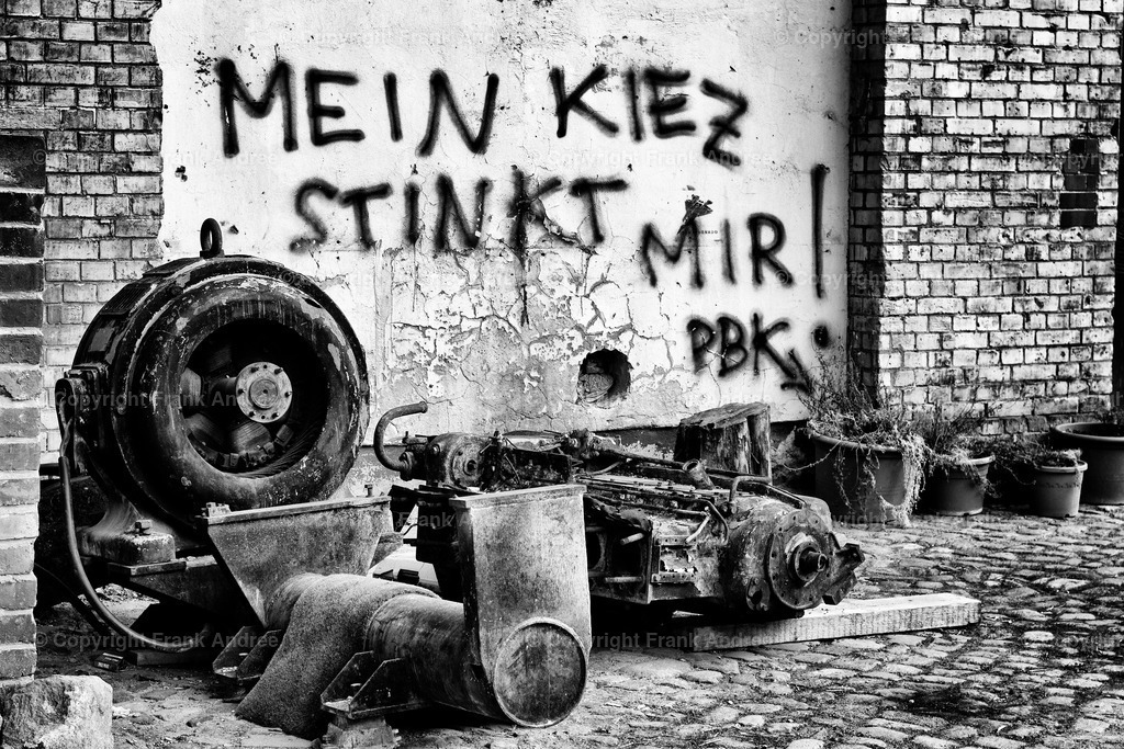 Berlin Prenzlauer Berg - Mein Kiez | Graffiti an einer alten Hauswand hinter verrosteten Maschinenteilen in Berlin Prenzlauer Berg. Straßenfotografie aus Berlin schwarz und weiß. - Realisiert mit Pictrs.com