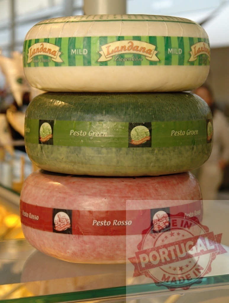 Landana cheese wheels stacking in deli display | Landana cheese varieties, including Pesto Green and Pesto Rosso, stack on a glass shelf - Realized with Pictrs.com