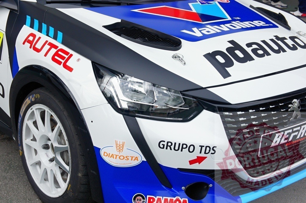 Peugeot 208 rally car showcasing sponsors at a motorsport event | Close-up of a Peugeot 208 rally car displaying various sponsor logos, highlighting the commercial aspect of motorsport - Realized with Pictrs.com