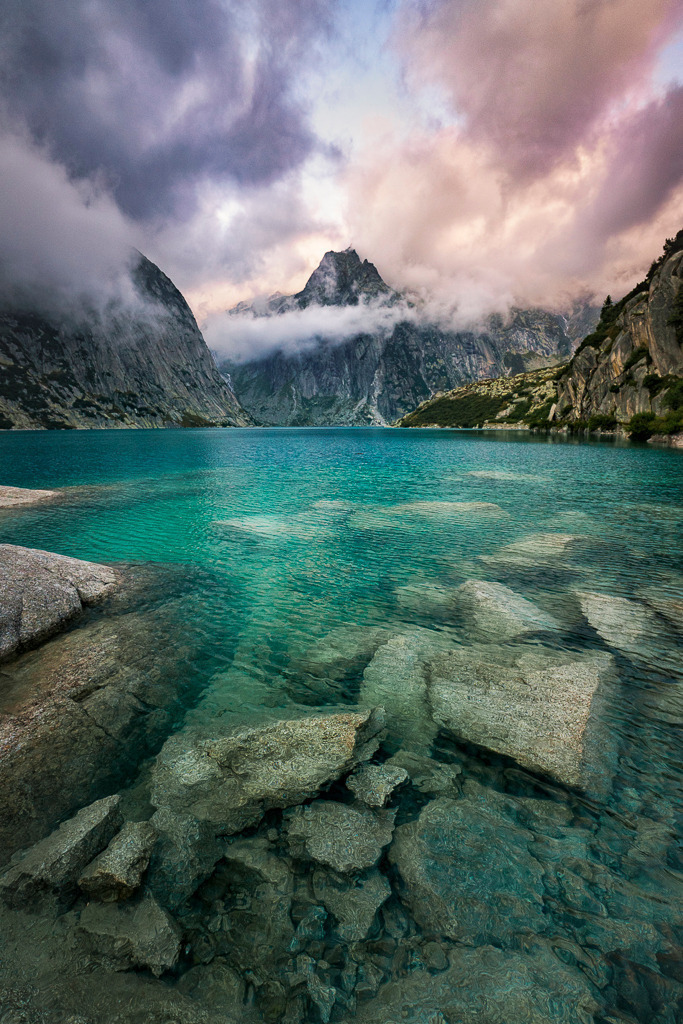 Mystischer Moment am Gelmersee | Türkisblaues Gletscherwasser, dramatische Wolken und eine eindrucksvolle Bergkulisse: Der Gelmersee im Wallis zeigt sich hier von seiner wild-romantischen Seite. Die Steine im klaren Wasser verleihen dem Bild Tiefe und Struktur. - Realisiert mit Pictrs.com