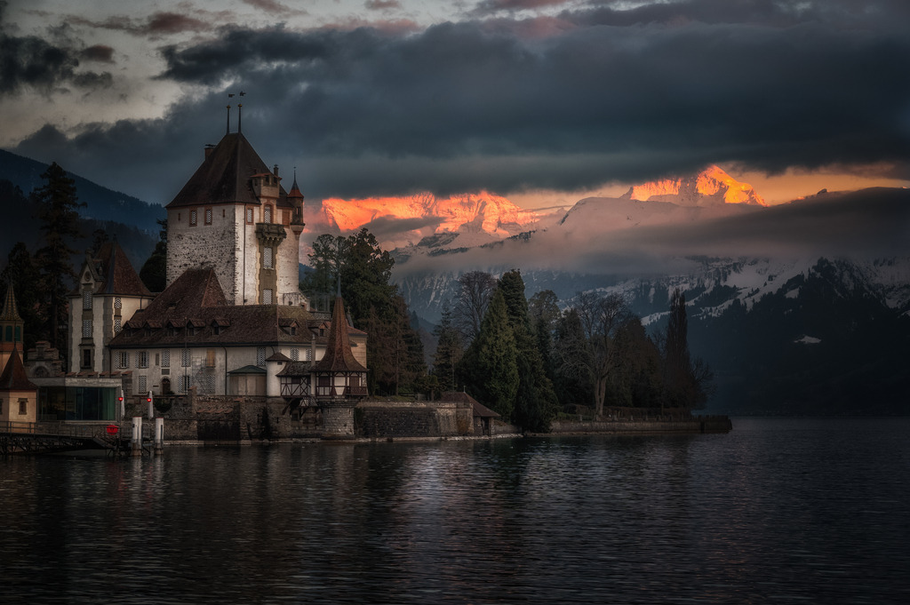 Peepshow | Schloss Oberhofen am Thunersee; im Hintergrund öffnet sich ein Fenster in der Wolkendecke und gibt den Blick frei auf die Berner Alpen im Abendrot. 
------------------------------------------------------------
Oberhofen Castle on Lake Thun; In the background a window opens in the cloud cover and offers a view of the Bernese Alps in the sunset.
------------------------------------------------------------
Dieser Druck ist in einer limitierten Auflage von 5 Exemplaren erhältlich. 
This print is available in a limited edition of 5 copies. 
http://art.hess.photography/105-peepshow.html - Realisiert mit Pictrs.com