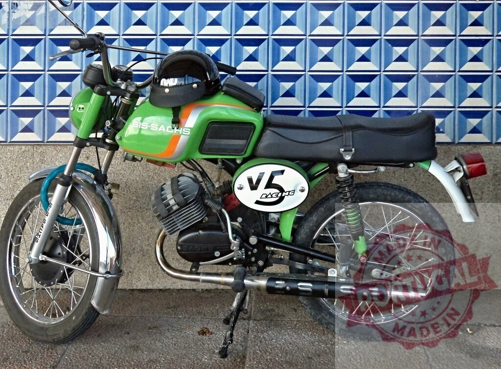 Green SIS-SACHS V5 Racing Motorcycle Parked Against Blue Tiled Wall | Classic green SIS-SACHS V5 Racing motorcycle parked against a vibrant blue tiled wall, showcasing vintage design and racing heritage - Realized with Pictrs.com