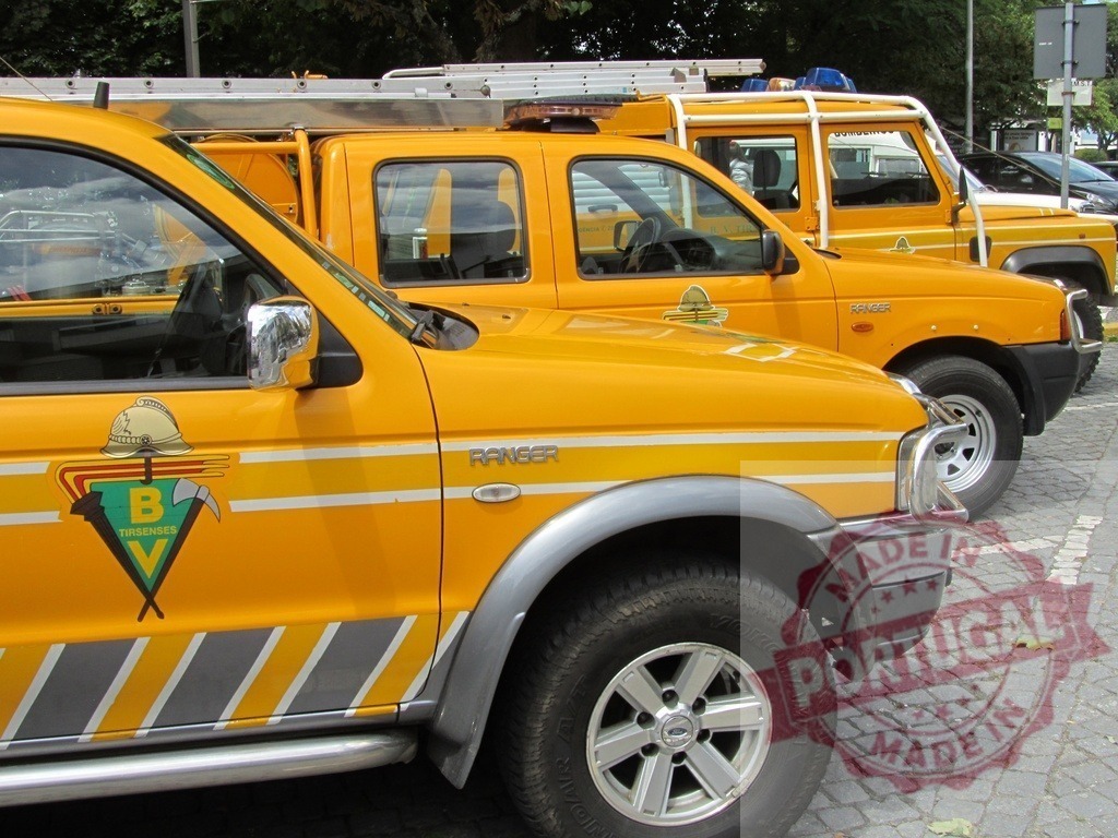 Ford Ranger and emergency vehicles parked on street | Yellow Ford Ranger pickup trucks and emergency vehicles parked during public event - Realized with Pictrs.com