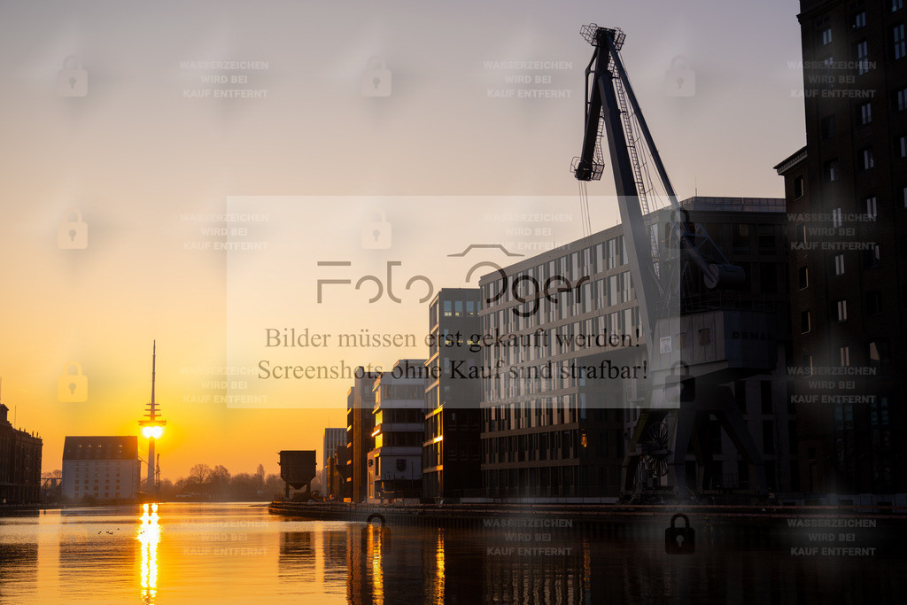 Morgengold im Hafen – Sonnenaufgang über der Stadt | Die ersten Sonnenstrahlen brechen über den stillen Hafen und tauchen Kräne, Speichergebäude und Wasser in ein warmes, goldenes Licht.Ein Moment der Ruhe zwischen Industrie und Moderne – festgehalten in einer Szene, die den Zauber des frühen Morgens spürbar macht. - Realisiert mit Pictrs.com