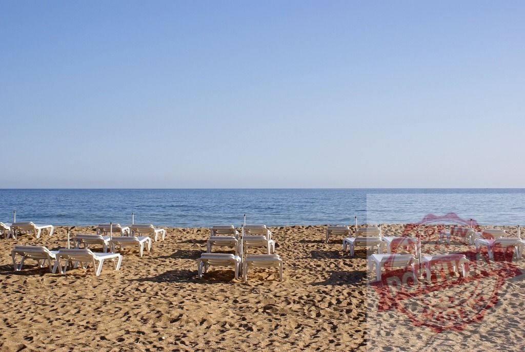 Empty sand beach with white lounge chairs and ocean | Empty white lounge chairs on a sandy beach looking out at the calm blue ocean - Realized with Pictrs.com