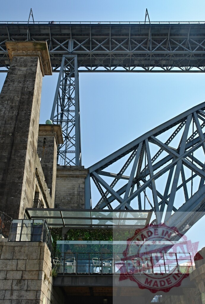 Dom Luís I Bridge architecture featuring steel structure and café. Porto - Portugal | Dom Luís I Bridge steel arch and truss construction rising above a modern glass café - Realisiert mit Pictrs.com