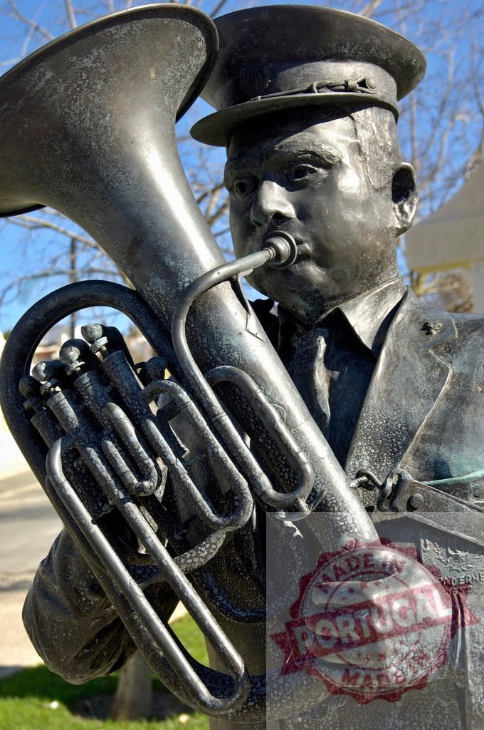Bronze musician statue playing a tuba on city street | Bronze statue of a musician in uniform playing a tuba on a street - Realisiert mit Pictrs.com