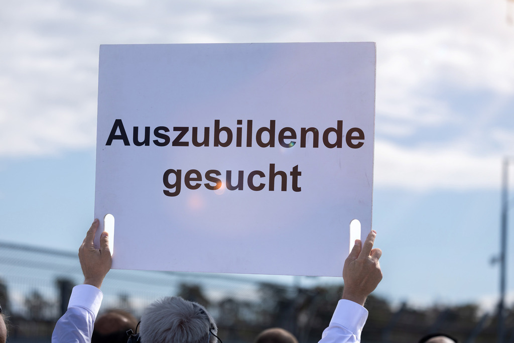 AUSZUBILDENDE GESUCHT Schild | (Fotomontage) Ein Schild mit dem Text AUSZUBILDENDE GESUCHT wird in die Höhe gehalten - Realisiert mit Pictrs.com