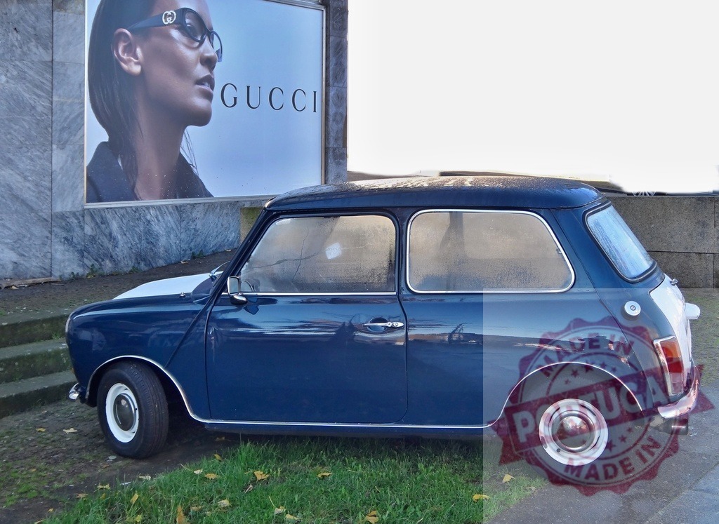 Blue vintage Mini Cooper parking near Gucci billboard | Blue classic Mini Cooper parked on grass next to a fashion advertisement billboard - Realized with Pictrs.com
