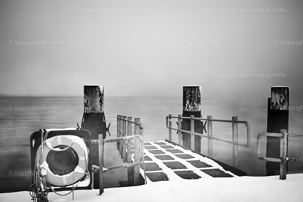 Landungssteg im Winter | Ein schneebedeckter Steg im Winter an der Ostsee im Nebel., schwarz-weiss. - Realisiert mit Pictrs.com