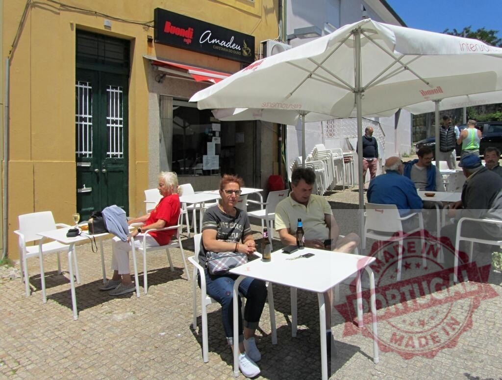 People relaxing at outdoor café tables in sunlight | People enjoying drinks and conversation at an outdoor cafe with white tables and umbrellas - Realized with Pictrs.com