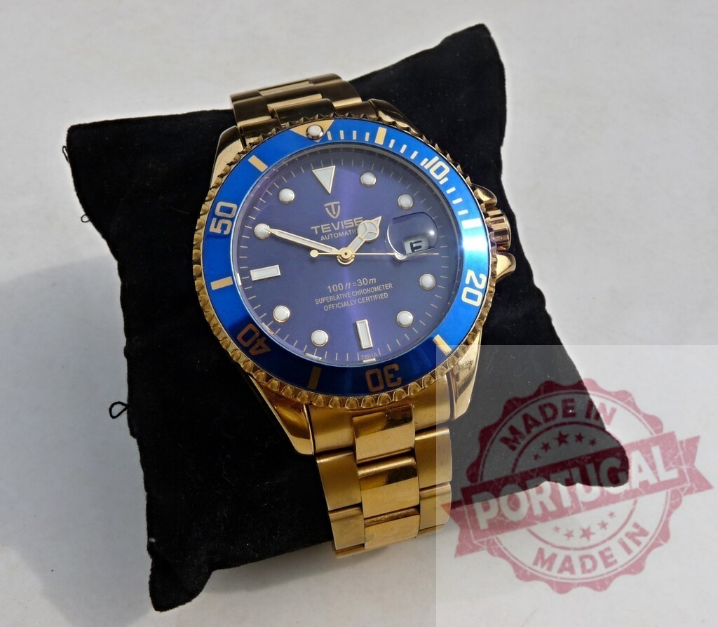 Tevise automatic gold watch with blue bezel on pillow | Tevise automatic gold-plated wrist watch with blue dial and bezel resting on a black velvet pillow - Realisiert mit Pictrs.com