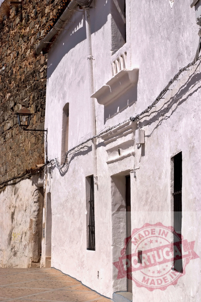 Old white plastered building and stone wall on street. Extremdura - Spain | Traditional architecture with textured white facade and rustic stone creating a contrast - Realized with Pictrs.com