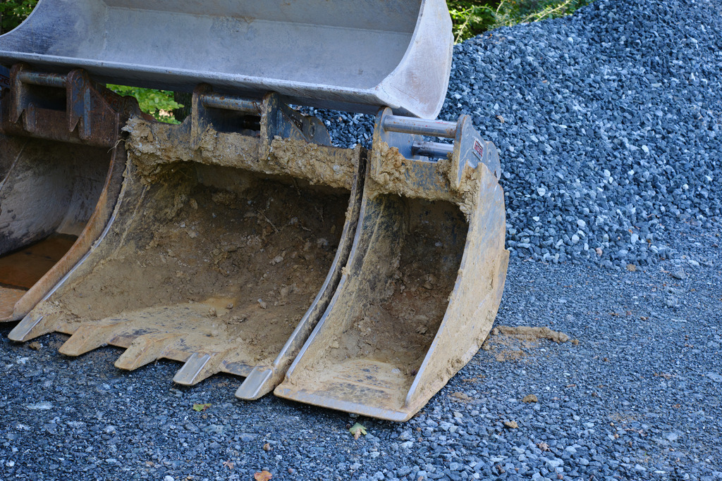 Kieshaufen und Baggerschaufel am Rand der Strasse | Burgenland, Austria - August 11, 2023: Kieshaufen und abgestellte Baggerschaufel am Rand der Strasse. - Realisiert mit Pictrs.com