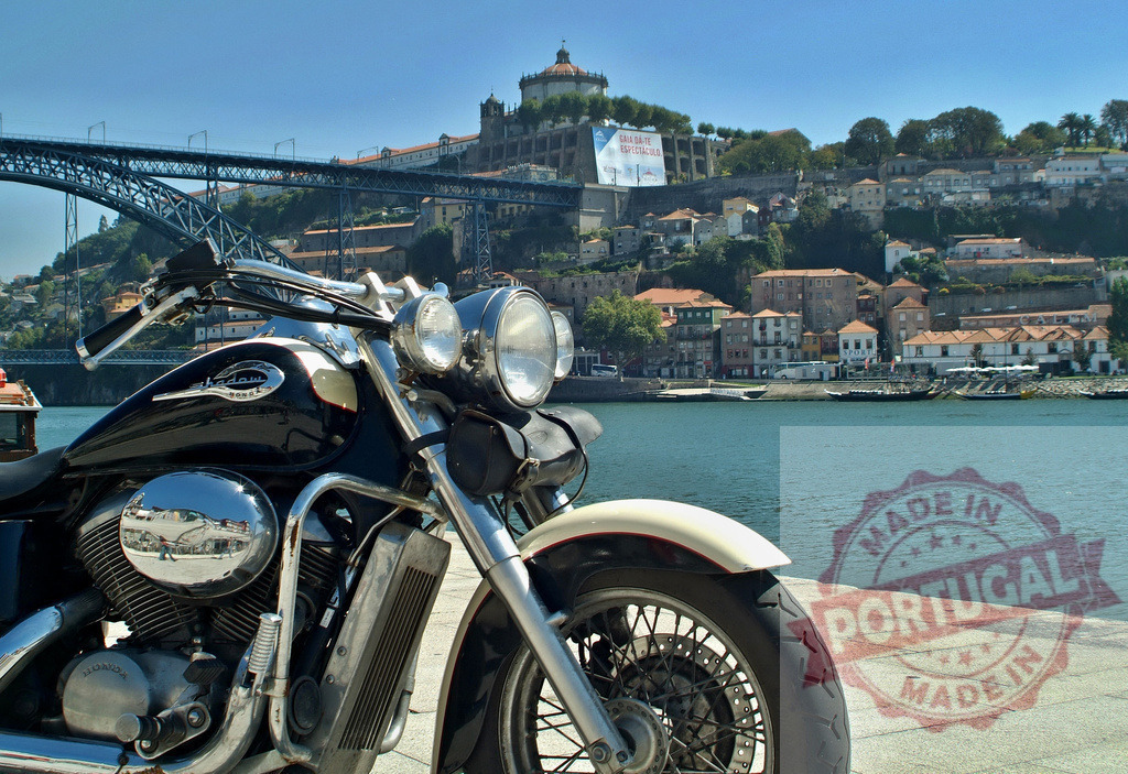 Motorcycle parked by Douro river in Porto city | Cruiser motorcycle parked by the Douro river with Porto cityscape and Dom Luís I Bridge - Realisiert mit Pictrs.com