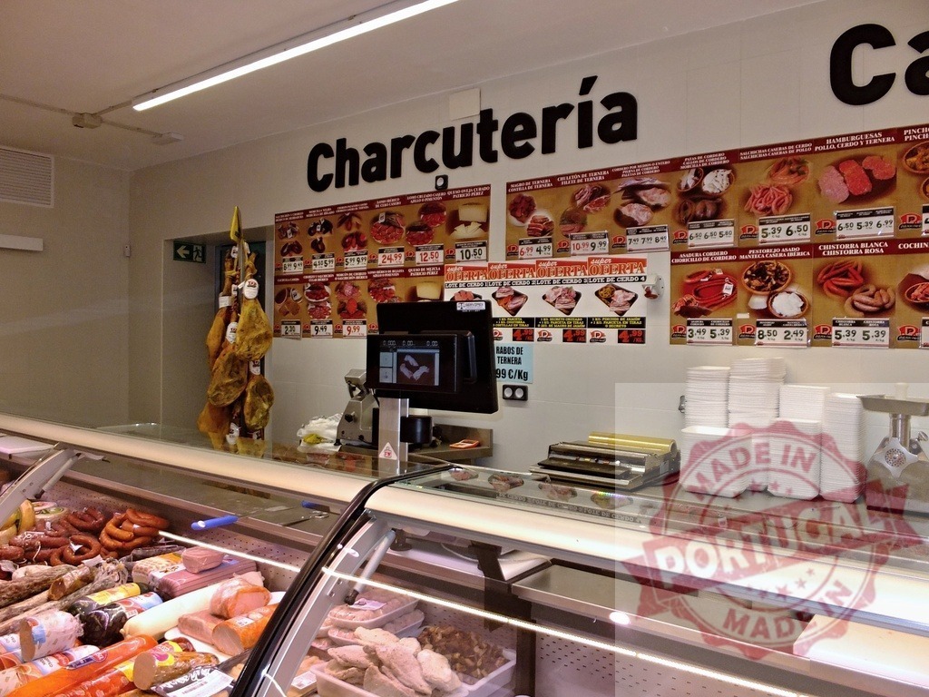 Charcutería displaying cured meats and weighing scale | Charcutería counter showcasing various cured meats, sausages, and hams for sale - Realisiert mit Pictrs.com
