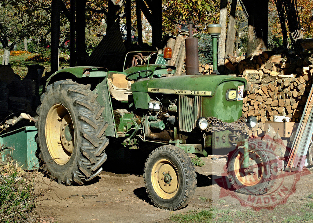 John Deere 2020 tractor in rustic farm setting | Green John Deere 2020 tractor sitting outdoors next to a stacked woodpile on a farm - Realisiert mit Pictrs.com