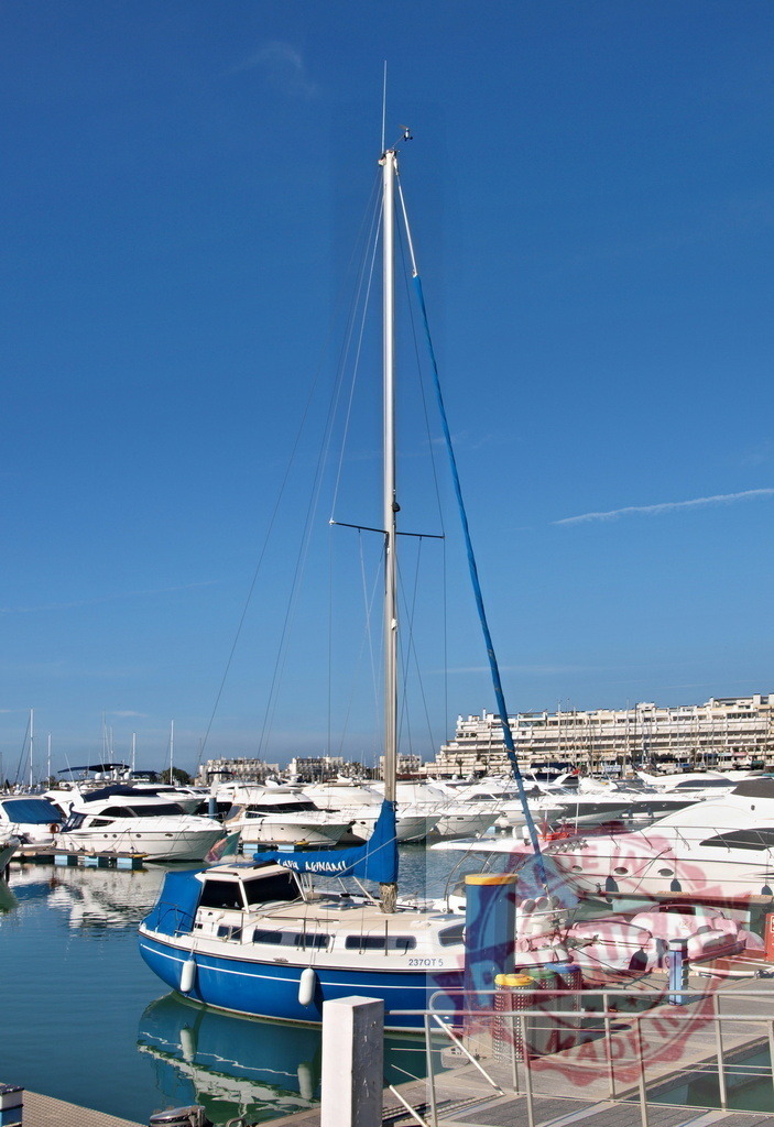 Sailboat and luxury yachts moored in Vilamoura marina | Blue sailboat and boats docked in a busy marina under a clear blue sky - Realized with Pictrs.com