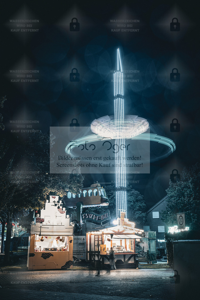Lichterturm auf der Kirmes – Nachtaufnahme in leuchtendem Blau | Ein Moment voller Licht und Bewegung: Der leuchtende Turm auf der Kirmes zieht die Blicke in den Nachthimmel, während im Vordergrund die Buden warm erstrahlen.Regenreflexe und Lichtspuren verleihen dem Bild eine fast magische Tiefe – ein Stück Kirmesnostalgie, eingefangen in einer stillen Nacht.Ideal für alle, die urbane Nachtstimmungen und das besondere Flair von Volksfesten lieben. - Realisiert mit Pictrs.com