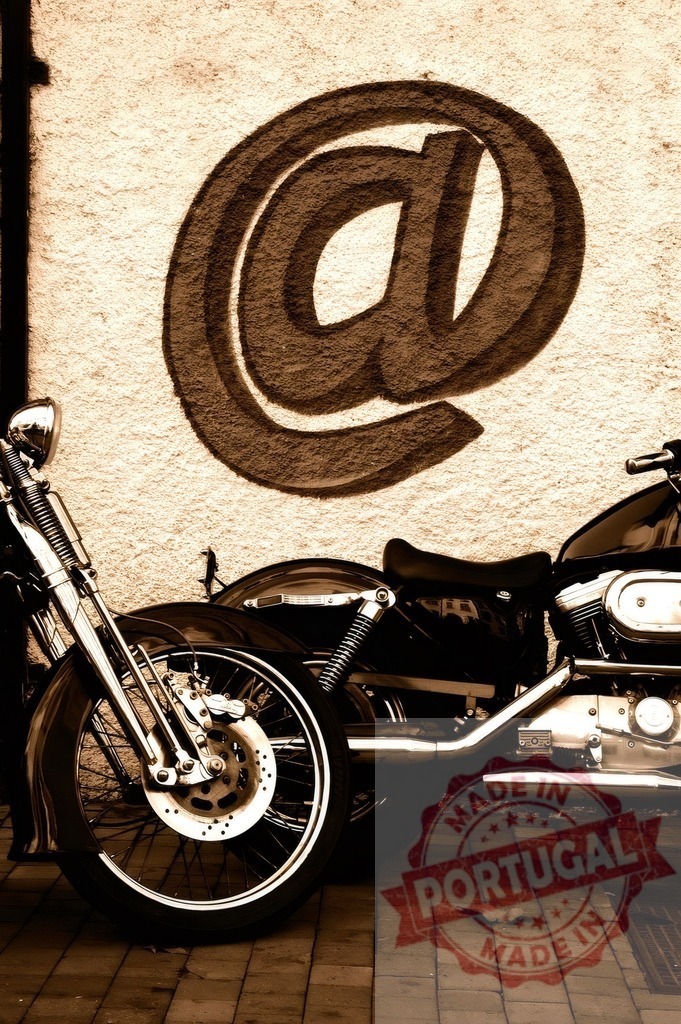 Motorcycle parked in front of at symbol graffiti | Custom motorcycle parked against a wall with a sepia-toned at symbol graffiti design - Realized with Pictrs.com