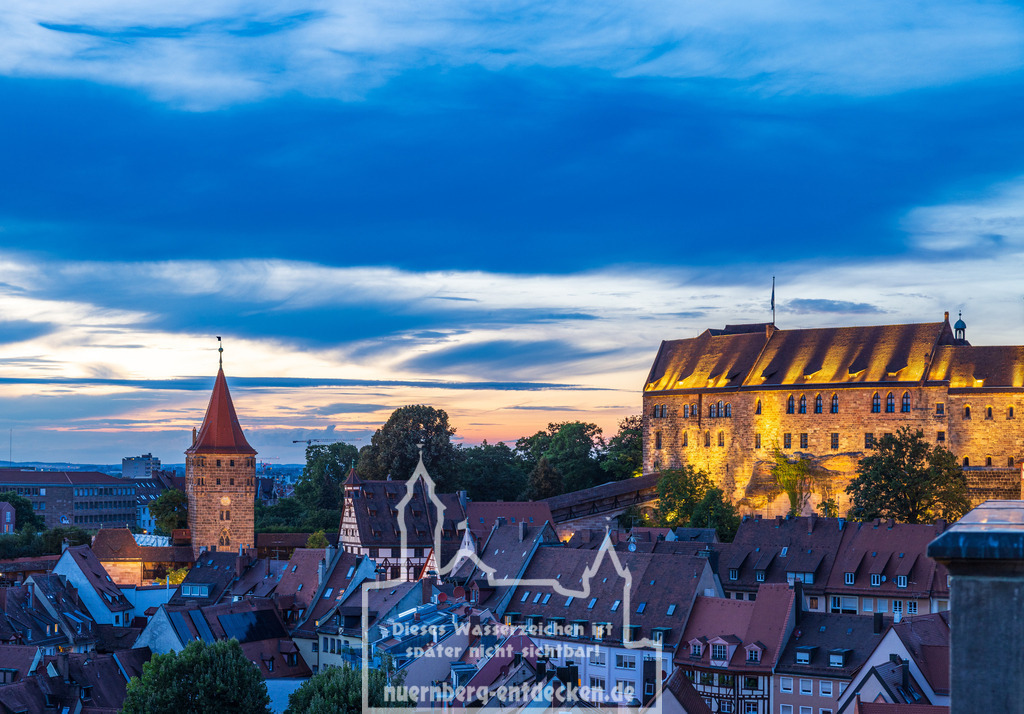 Nürnberger Stadtbild am Abend | Blick auf das Tiergärtnertor und den beleuchteten Palas der Kaiserburg in Nürnberg während der Dämmerung. Die historischen Gebäude erstrahlen im warmen Licht, während der Himmel in Blau- und Orangetönen leuchtet und den Sonnenuntergang über der Stadt einrahmt. - Realisiert mit Pictrs.com