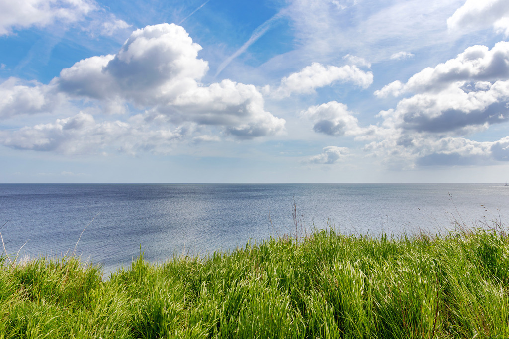 Wandbild: Grünes Gras und Blaues Meer  | Die unberührte Schönheit der Ostseeküste – dieses Wandbild zeigt den weiten Blick von der Steilküste in Schönhagen auf das offene Meer. Im Vordergrund wiegt sich das Gras sanft im Wind, während sich der blaue Himmel mit frühlingshaften, leichten Wolken über die Küstenlandschaft erstreckt. Die harmonische Szene schafft ein Gefühl von Ruhe und Freiheit – perfekt für alle, die sich eine maritime Atmosphäre in ihr Zuhause holen möchten. - Realisiert mit Pictrs.com