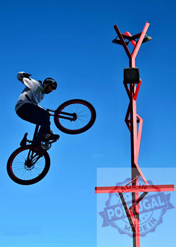 Cyclist performing a trick with his bike in a skate park | Bmx rider jumping with his bike in a skate park with a clear blue sky - Realized with Pictrs.com