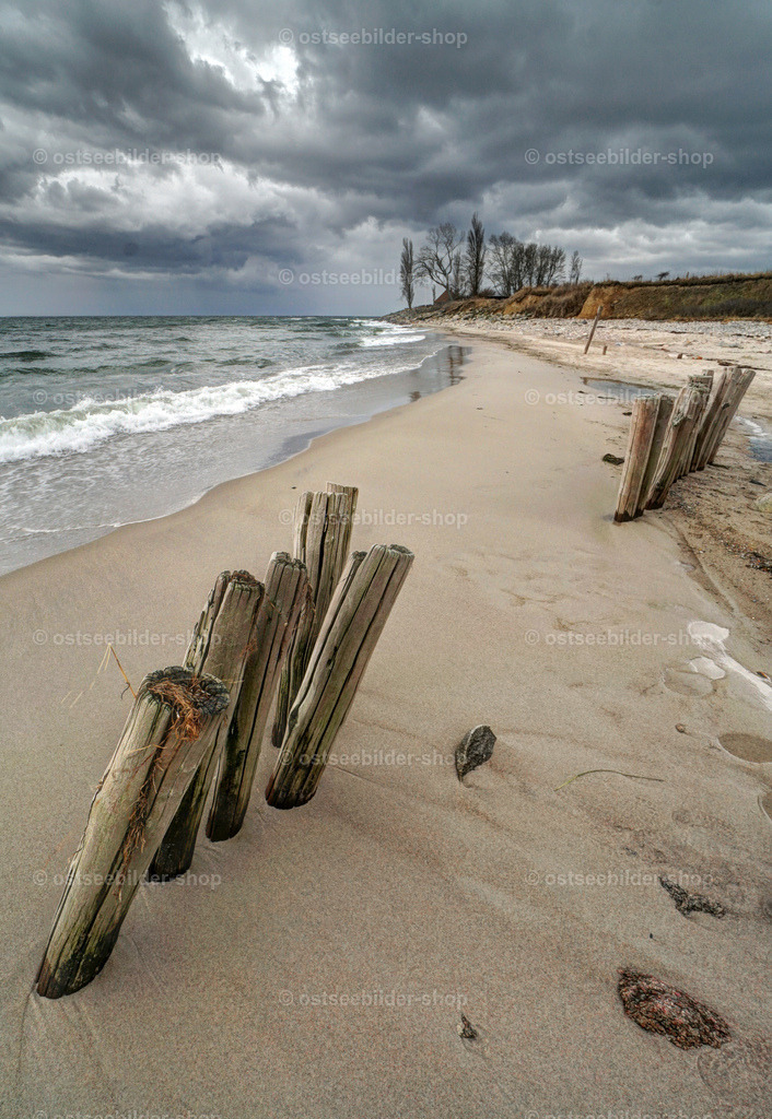 Regentag an der Küste | Dunkle Regenwolken nähern sich rasch einem Strand mit Resten eines alten, hölzernen Wellenbrechers.