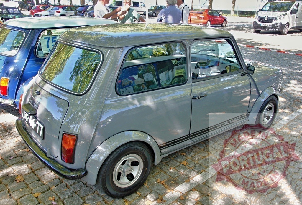 Gray Mini 1275 GT parked on cobblestone street during vintage car meeting | Classic Mini 1275 GT parked on a cobblestone street during a vintage car exhibition, with visitors and other classic cars in the background - Realized with Pictrs.com