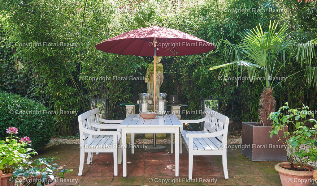 Mediterraner Stadtgarten | asiatisch anmutende Terrasse mit weißen Gartenmöbeln und rotem Sonnenschirm - Realisiert mit Pictrs.com