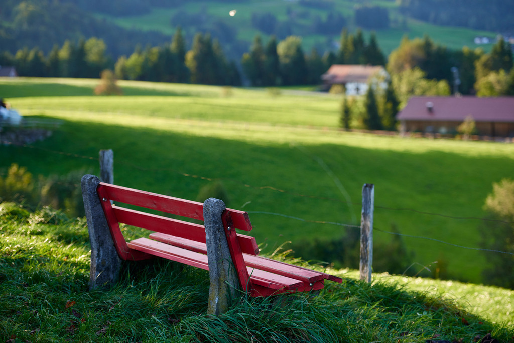 Blick in die Bregenzerwälder Landschaft | Bildstein, Austria - September 14, 2017: Blick in die Bregenzerwälder Landschaft, im Vordergrund eine rote Sitzbank. - Realisiert mit Pictrs.com