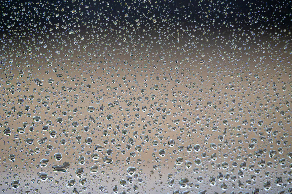 Perlen des Regens am Fenster | Unzählige glitzernde Wassertropfen überziehen eine Fensterscheibe wie ein fein gewebtes Netz. Dahinter verschwimmt das sanfte, warme Licht des Tages in einem weichen, melancholischen Farbverlauf von sanftem Ocker bis hin zu einem kühlen Dunkelblau. Die Nahaufnahme fängt die stille Geborgenheit eines verregneten Tages ein – das ruhige Gefühl, dem Prasseln des Wetters von drinnen zuzusehen. Ein abstraktes, zeitloses Motiv voller Poesie, das die friedliche Seite eines Wetterwechsels spürbar macht. - Realisiert mit Pictrs.com