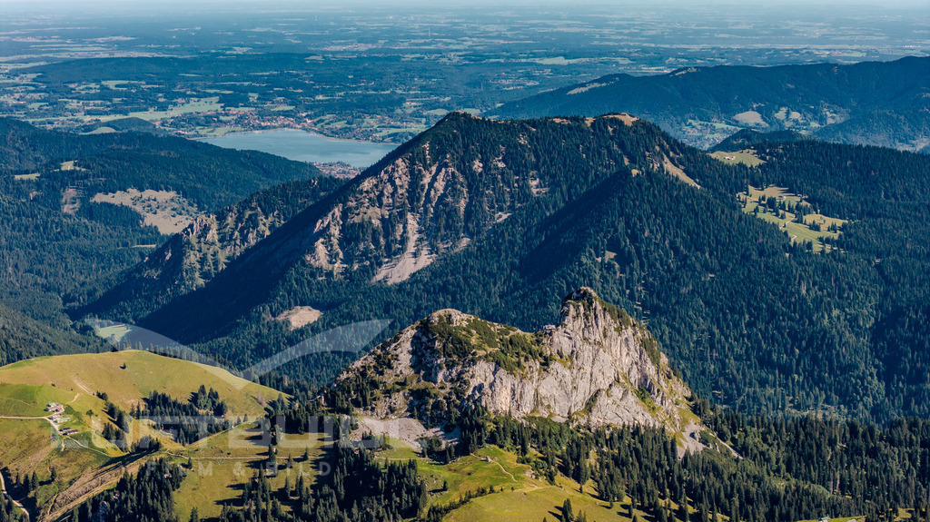 Roß- und Buchstein vor dem Hirschberg | Ein Blick, der begeistert: Im Vordergrund thronen Roß- und Buchstein mit ihrer markanten Silhouette. Dahinter erhebt sich der Hirschberg. Auch hier täuscht die Perspektive, denn allesamt sind die Gipfel um die 1650 m ü. NN, doch hier dominiert eindeutig der Hirschberg. Und am Horizont glitzert der Tegernsee wie ein Versprechen. - Realisiert mit Pictrs.com