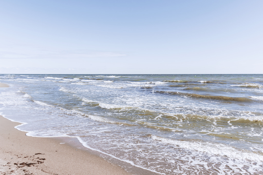 XXL Wandbild: Kleine Wellen am Ostseestrand | Maritime Weite und nordische Frische im Querformat. Dieses XXL Wandbild fängt die klassische Schönheit der Ostsee in einem hellen, klaren Moment ein: Der Blick gleitet über den nassen Sand am Uferrand hin zu den sanft auslaufenden Wellen. Ein weiter, blau-weißer Himmel über dem offenen Meer unterstreicht das Gefühl von Freiheit und Ruhe. Nutzen Sie dieses belebende Motiv in großzügigen Wohnbereichen, um eine offene und freundliche Atmosphäre zu schaffen. Die harmonische Farbpalette aus hellen Sandtönen und dem strahlenden Blau des Wassers verleiht jeder Wand eine erfrischende Tiefe. Auch für moderne Büros oder Ferienwohnungen ist dieser Ausblick ideal, um eine Atmosphäre von Weite und Entspannung zu vermitteln.