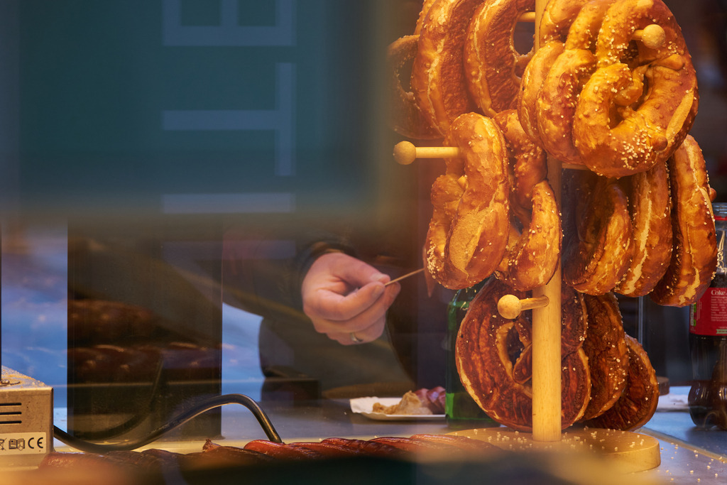 Blick in einen Imbisstand mit Bratwurst und Brezel | Wien, Austria - November 18, 2025: Blick in einen Imbisstand mit Bratwurst und Brezel; ein Kunde isst Currywurst. - Realisiert mit Pictrs.com
