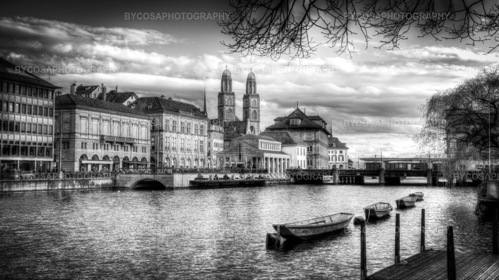 Timeless Zürich _ Grossmünster in Black _ White | Eine ruhige Schwarz-Weiß-Fotografie in FineArt-Qualität fängt eine der bekanntesten Ansichten Zürichs ein: die friedlich dahingleitenden Boote auf der Limmat und die historische Architektur der Altstadt mit dem Grossmünster im Hintergrund. Die monochromen Töne unterstreichen die Eleganz, Tiefe und den zeitlosen Charakter der Stadt und schaffen ein Kunstwerk, das sich perfekt in moderne, minimalistische und luxuriöse Interieurs einfügt. - Realisiert mit Pictrs.com