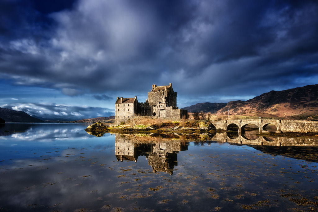 Eilean Donan Castle, Schottland | Eilean Donan Castle in Schottland, Spiegelung im Wasser.Das historische Eilean Donan Castle thront majestätisch auf seiner Insel, verbunden durch eine Steinbrücke. Dramatische dunkle Wolken kontrastieren mit blauen Himmelsabschnitten und erzeugen eine markante Spiegelung im ruhigen Wasser des Lochs. Die Komposition betont die ikonische Architektur des Schlosses und seine Integration in die raue schottische Landschaft.***### 10 tagsCastle, Scotland, Eilean Donan, Reflection, Landscape, Dramatic, History, Travel, Loch, Mountains - Realisiert mit Pictrs.com