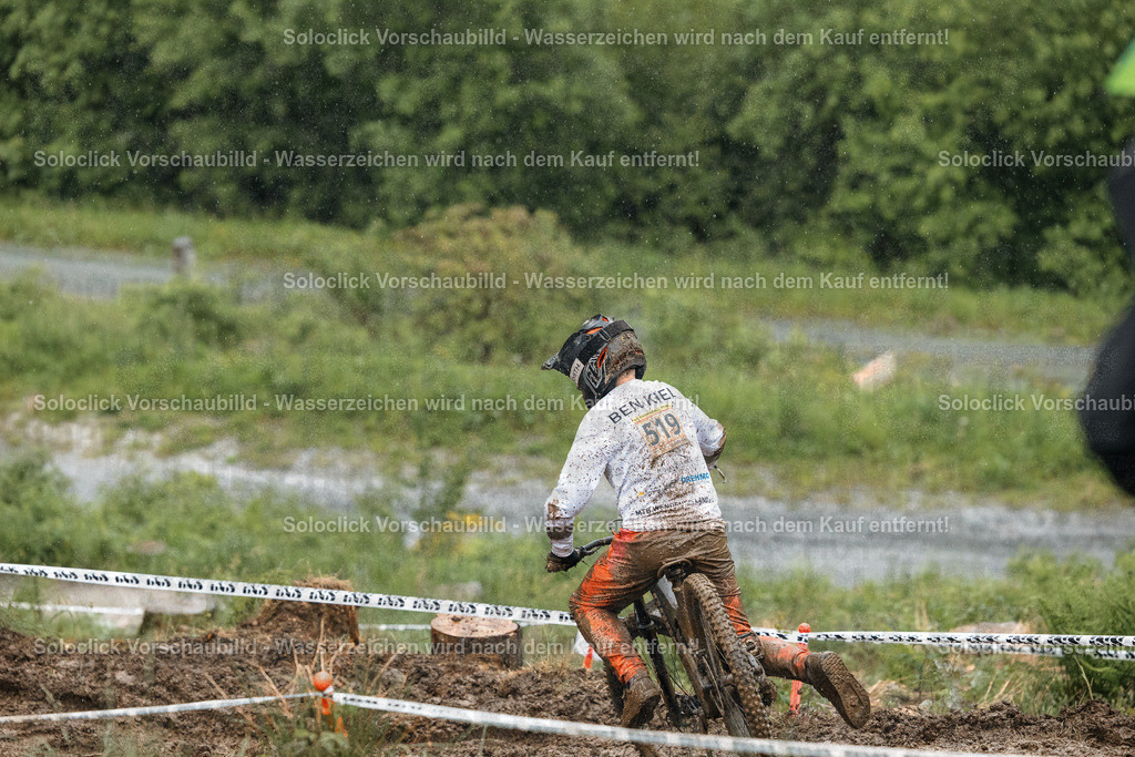 Schlammiger Kampf | Ein Mountainbiker in voller Ausrüstung, einschließlich Helm und Handschuhen, kämpft sich durch einen extrem schlammigen und anspruchsvollen Kurs. Er ist in voller Aktion, sein Körper ist angespannt und er scheint sich mit aller Kraft anzustrengen, um den Kurs zu bewältigen. Der Hintergrund zeigt eine verschwommene Landschaft mit Bäumen und Vegetation, die ebenfalls mit Schlamm bedeckt ist. Die Szene vermittelt ein Gefühl von Anstrengung, Entschlossenheit und Abenteuer. - Realisiert mit Pictrs.com