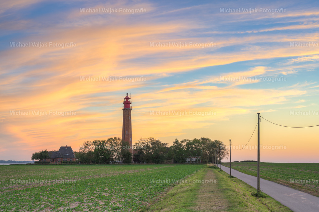 Leuchtturm Flügge auf Fehmarn bei Sonnenuntergang | Der Leuchtturm Flügge auf Fehmarn ist ein beliebtes Ausflugsziel für Besucher der Ostseeinsel. Er wurde 1915 erbaut und ist 37,5 Meter hoch. Von seiner Aussichtsplattform aus hat man einen herrlichen Blick über die Küste und das Meer. Der Leuchtturm ist noch in Betrieb und sendet alle 15 Sekunden ein weißes Lichtsignal aus. Er ist ein wichtiges Orientierungszeichen für die Schifffahrt in der Fehmarnbelt-Region. - Realisiert mit Pictrs.com