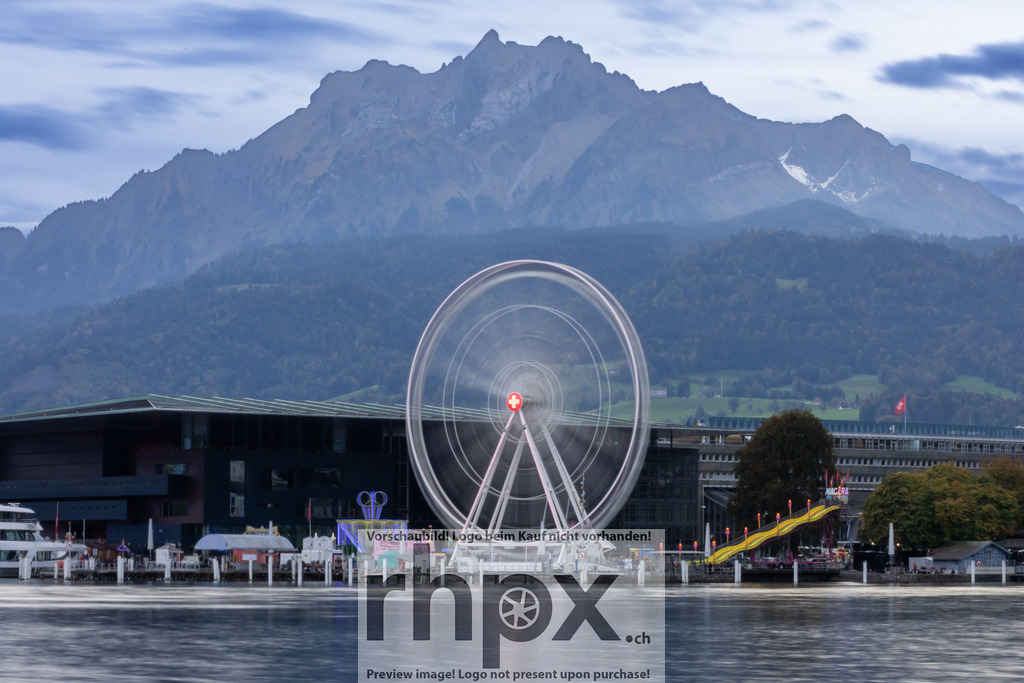 Riesenrad Luzern mit Pilatus im Hintergrund | Bewegung. Fels. Tradition.Das drehende Riesenrad der Luzerner Määs verschmilzt in dieser Aufnahme zu einem dynamischen Kreis vor der ewigen Ruhe des Pilatus. Ein faszinierender Kontrast zwischen flüchtigem Festmoment und majestätischer Bergwelt am Seeufer.Wähle unter "Produktauswahl" dein Wunschformat: Vom klassischen Wandbild über Puzzle &amp; Tassen bis zum digitalen Download (z.B. als Handy-Hintergrund). - Realisiert mit Pictrs.com