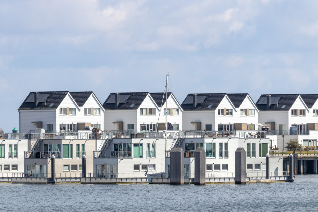 Wandbild: Ferienwohnungen in Olpenitz | Dieses Wandbild im Querformat zeigt zahlreiche Ferienwohnungen direkt am Meer in Olpenitz. Am Himmel sind zahlreiche Wolken zu sehen.  - Realisiert mit Pictrs.com