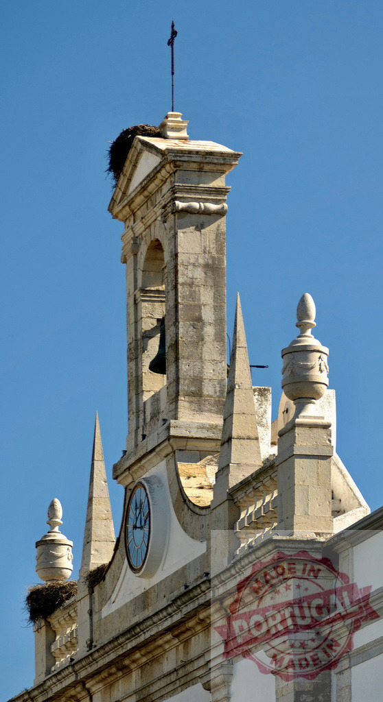 Arco da Vila Faro bell tower with stork nest and clock | Arco da Vila bell tower featuring a stork nest, bell, and clock against a clear blue sky - Realisiert mit Pictrs.com