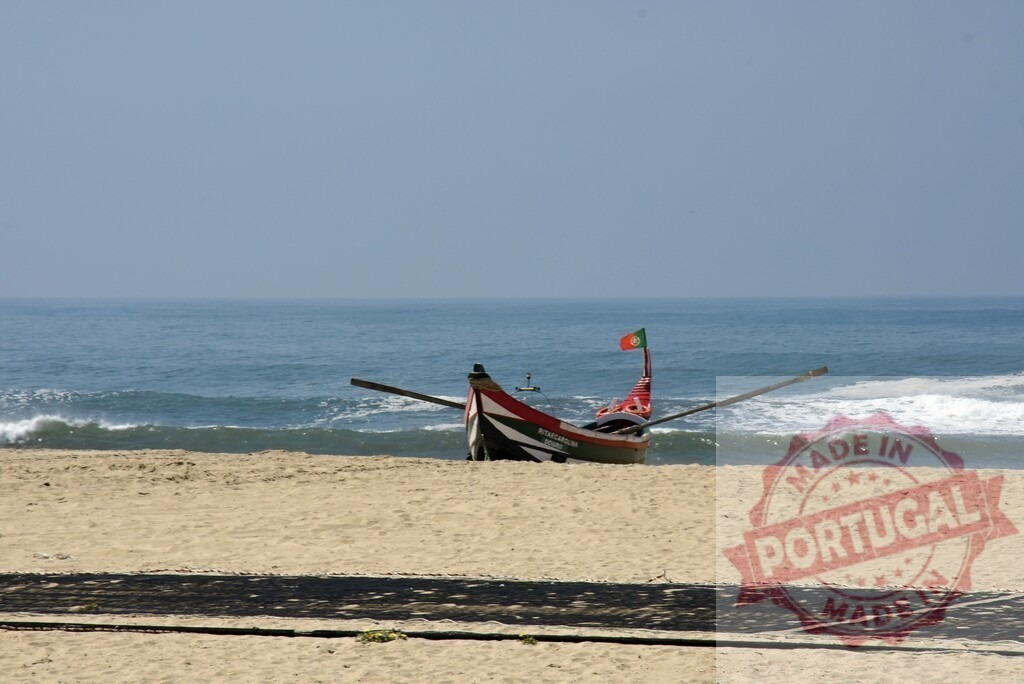 Aveiro Region - Portugal Fishing boat standing on a Portugal beach | Traditional fishing boat with a Portuguese flag resting on a sandy beach by the ocean - Realized with Pictrs.com