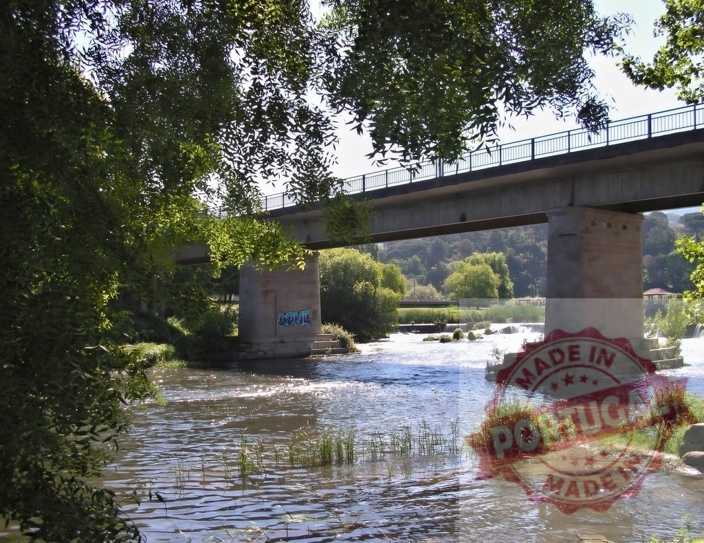 Concrete road bridge spanning a sunny river. Portugal - Norte | River flowing under a concrete bridge on a bright summer day with green trees - Realized with Pictrs.com