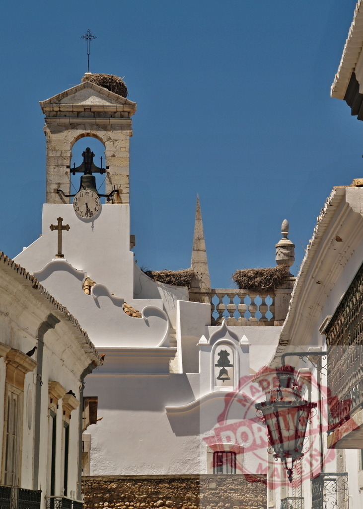 Faro cathedral bell tower with stork nest | Whitewashed architecture, clock and stork nest under clear blue sky - Realisiert mit Pictrs.com