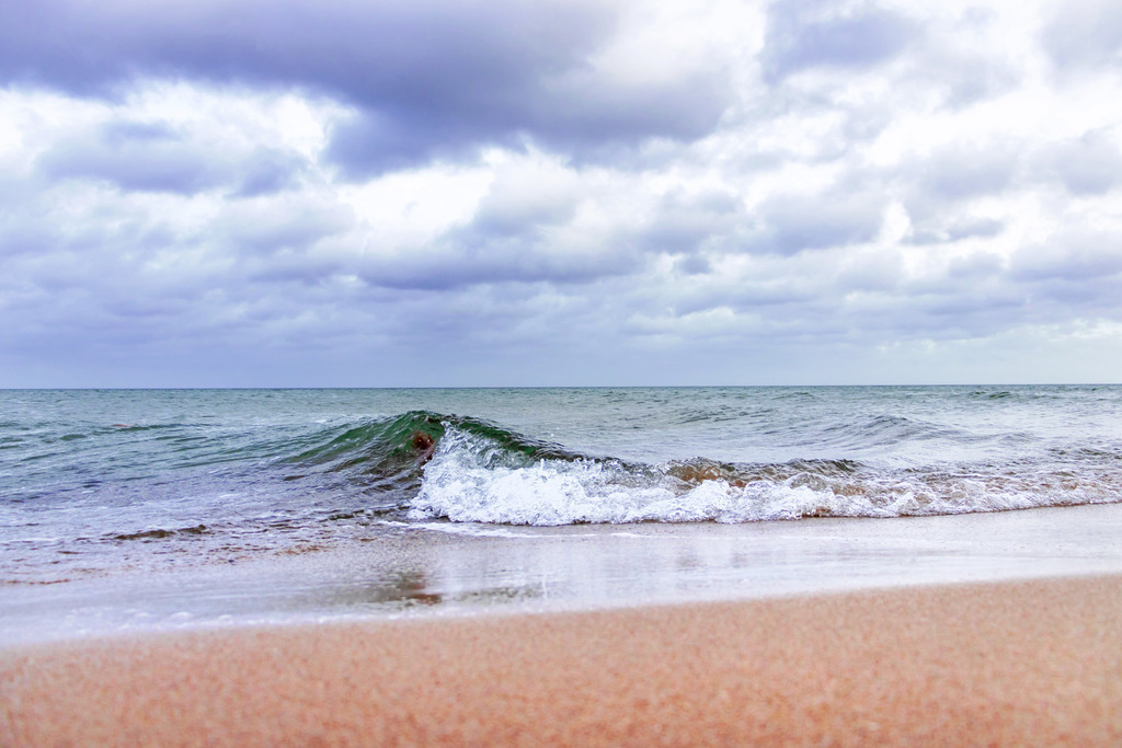 Wandbild: Einsame Welle am Ostseestrand | Genießen Sie die Ruhe und Gelassenheit am Weidefelder Ostseestrand mit diesem stimmungsvollen Wandbild im Querformat. Eine einzelne Welle bricht sanft am Ufer, während der Rest der Ostsee ruhig und friedlich daliegt. Der wolkenbedeckte Himmel und der sanfte Sandstrand im Vordergrund vermitteln eine beruhigende und harmonische Atmosphäre. - Realisiert mit Pictrs.com