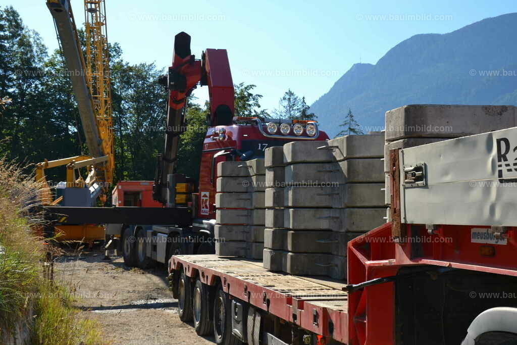 Kranaufbau | Einrichtung Baukran mit LKW-Kran der Sattelzugmaschine, davor LKW Tieflader mit Kranballast, dahinter Berge, weiß-blauer Himmel