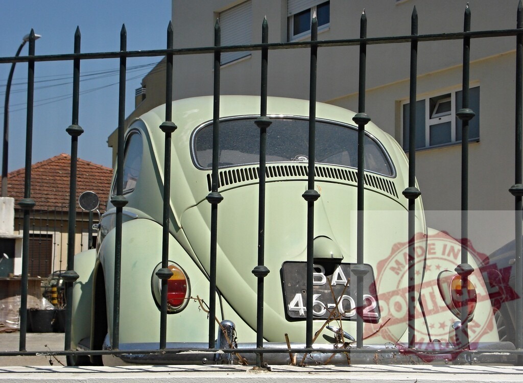 Classic Volkswagen Beetle Parked Behind Metal Fence | Rear view of a vintage Volkswagen Beetle seen through a metal fence, showcasing its iconic design and timeless appeal - Realized with Pictrs.com