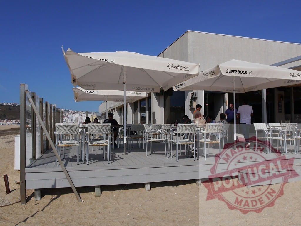 People relaxing at beach cafe outdoor restaurant in Foz do Arelho | Beachfront cafe patio with people sitting under umbrellas enjoying outdoor leisure - Realized with Pictrs.com